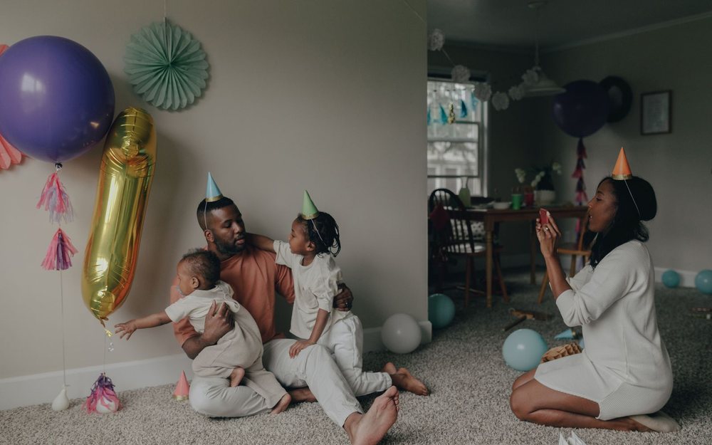 A family at a birthday party with balloons and party hats; a LIVE mark was added.