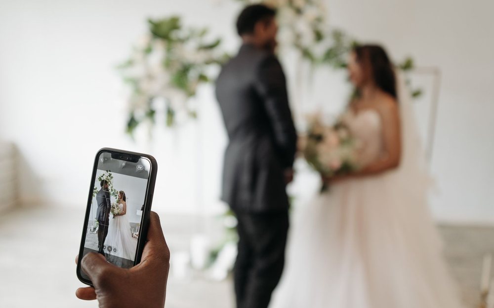 A hand holds a phone that films a couple at a wedding ceremony; a LIVE mark was added.