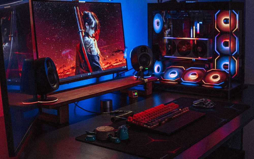 A dark gaming desk lit in red and blue with a monitor, a keyboard and a glass PC case; a LIVE mark was added to the photo.